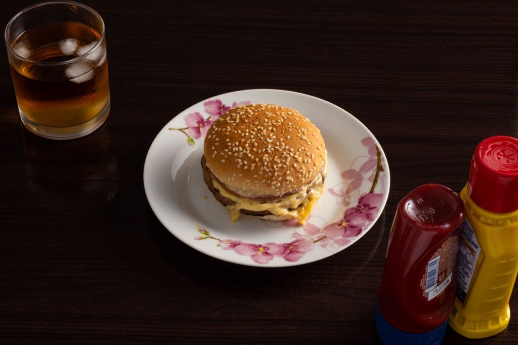 A cheeseburger with condiments and a drink on a dark wooden table.